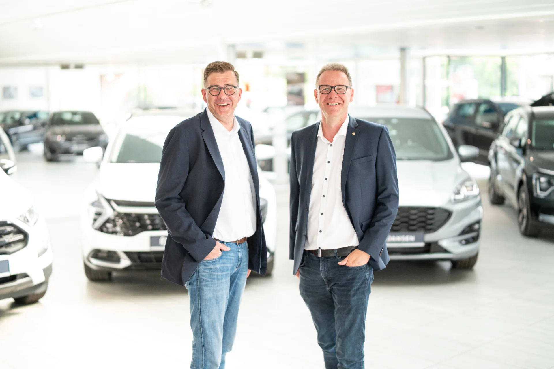 Two owners of Autohaus Jansen in the bright showroom with several vehicles